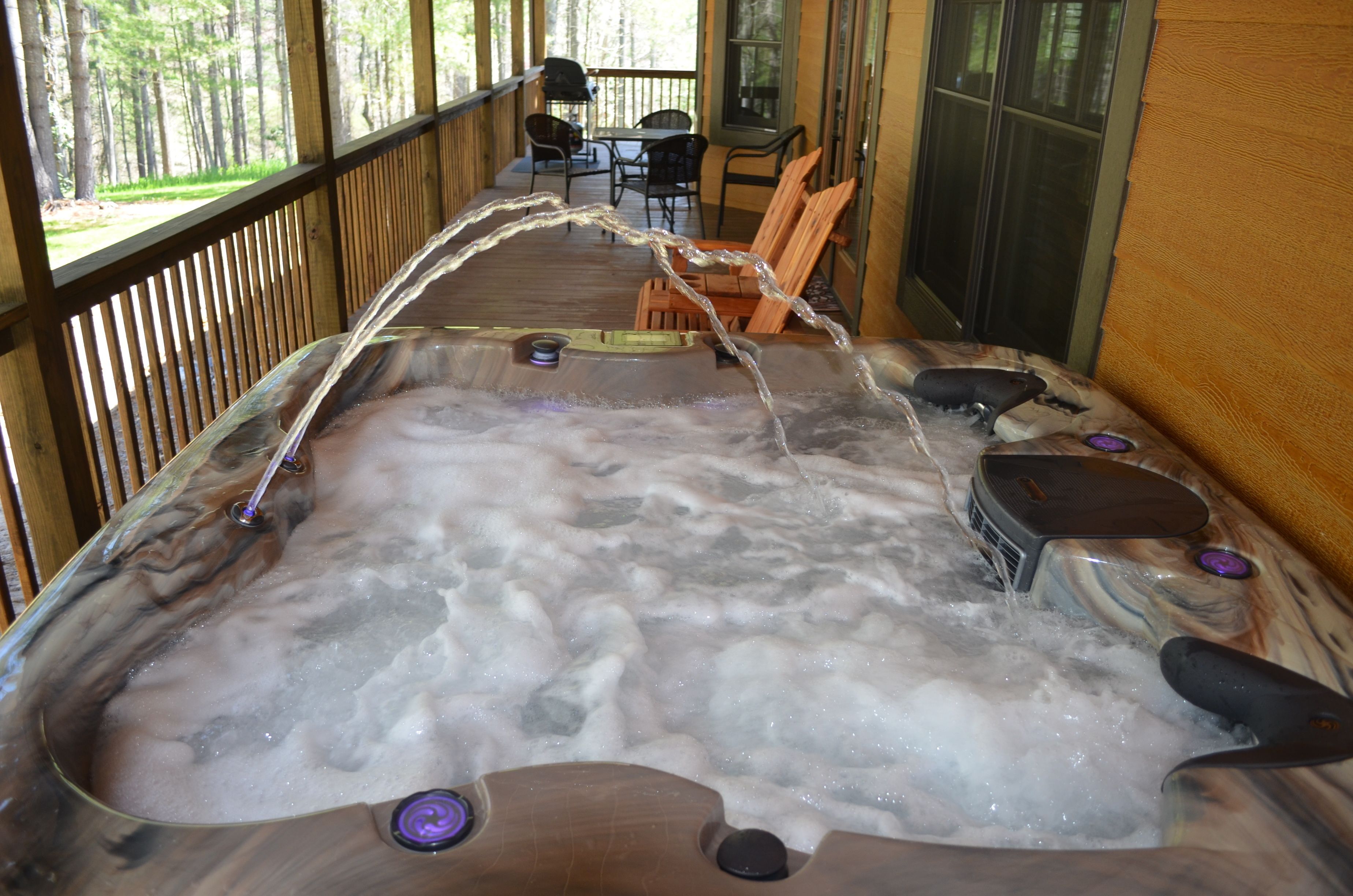 A hot tub with a wooden deck and a view of the surrounding forest.