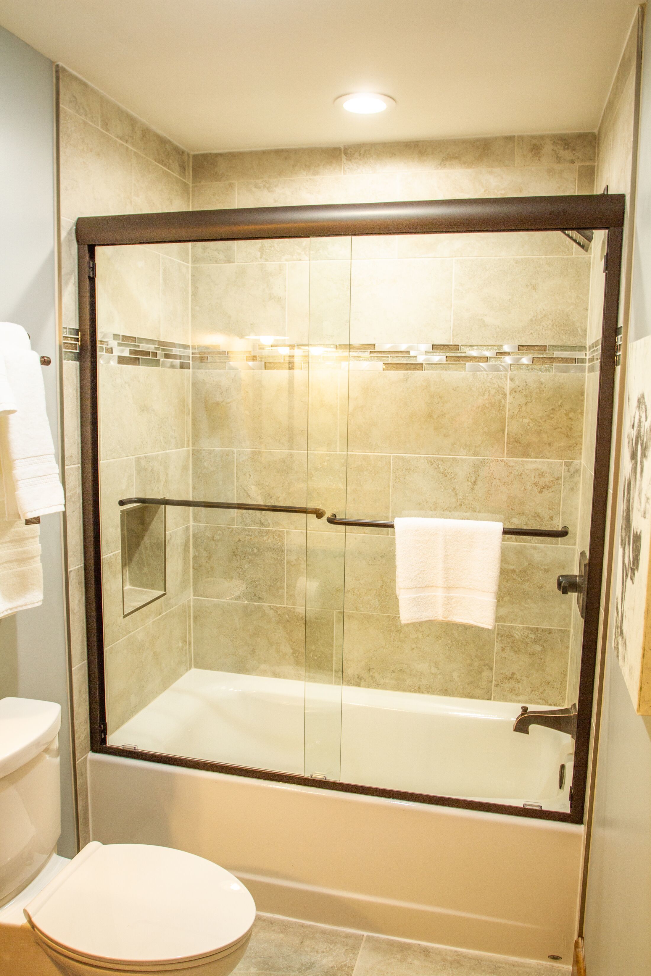 A glass-enclosed walk-in shower with a glass door, a white toilet, and a glass-enclosed bathtub.