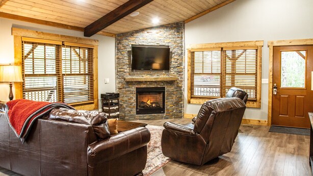 A cozy living room with a stone fireplace, leather sofas, and a flat-screen TV.