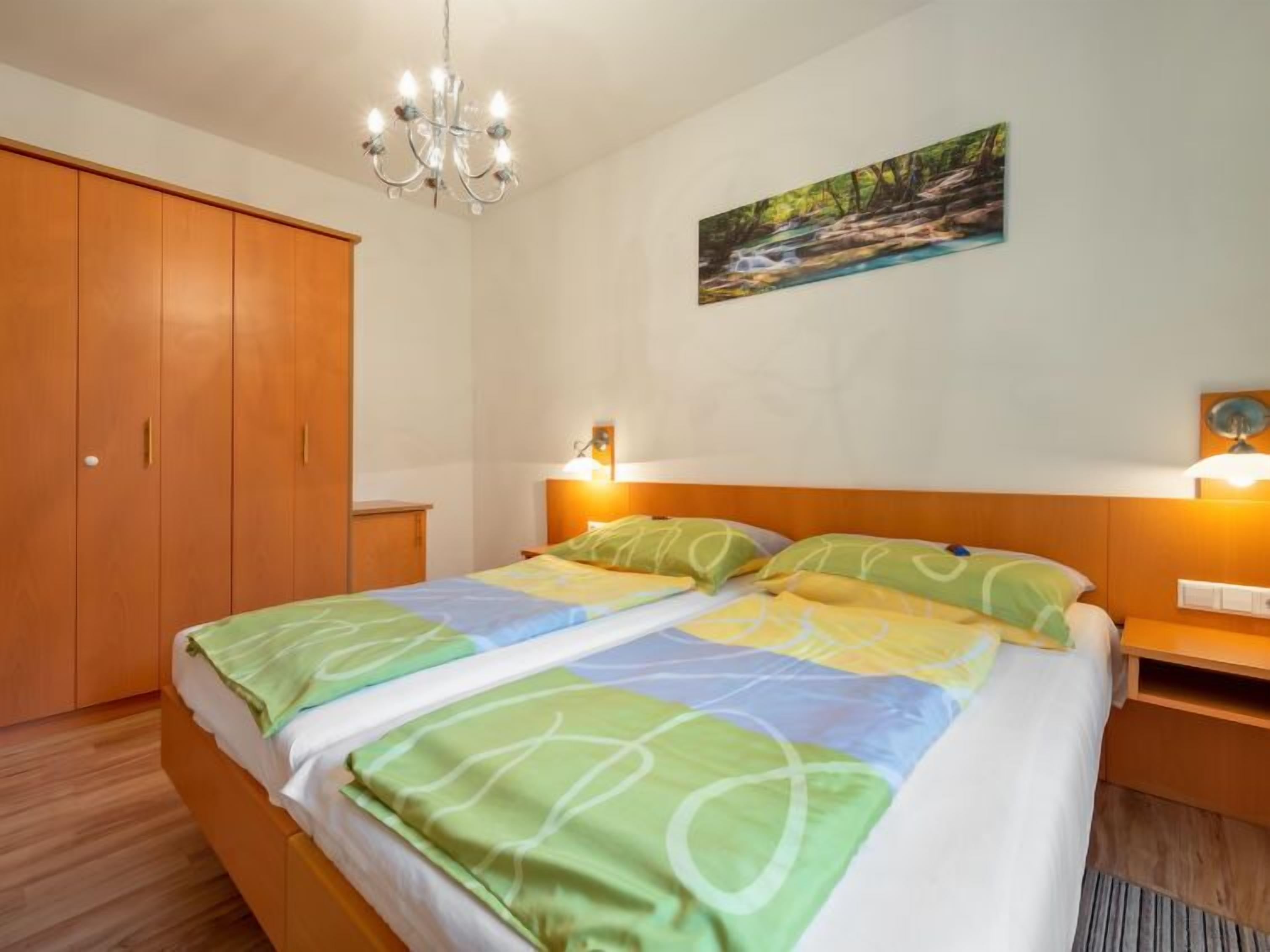 Een slaapkamer met een bed, een houten garderobe, een kroonluchter, wandlampen en een schilderij van een waterval.