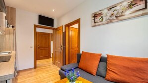 Uma sala de estar moderna com um sofá, uma mesa de centro com uma planta, piso de madeira e um quadro na parede.
