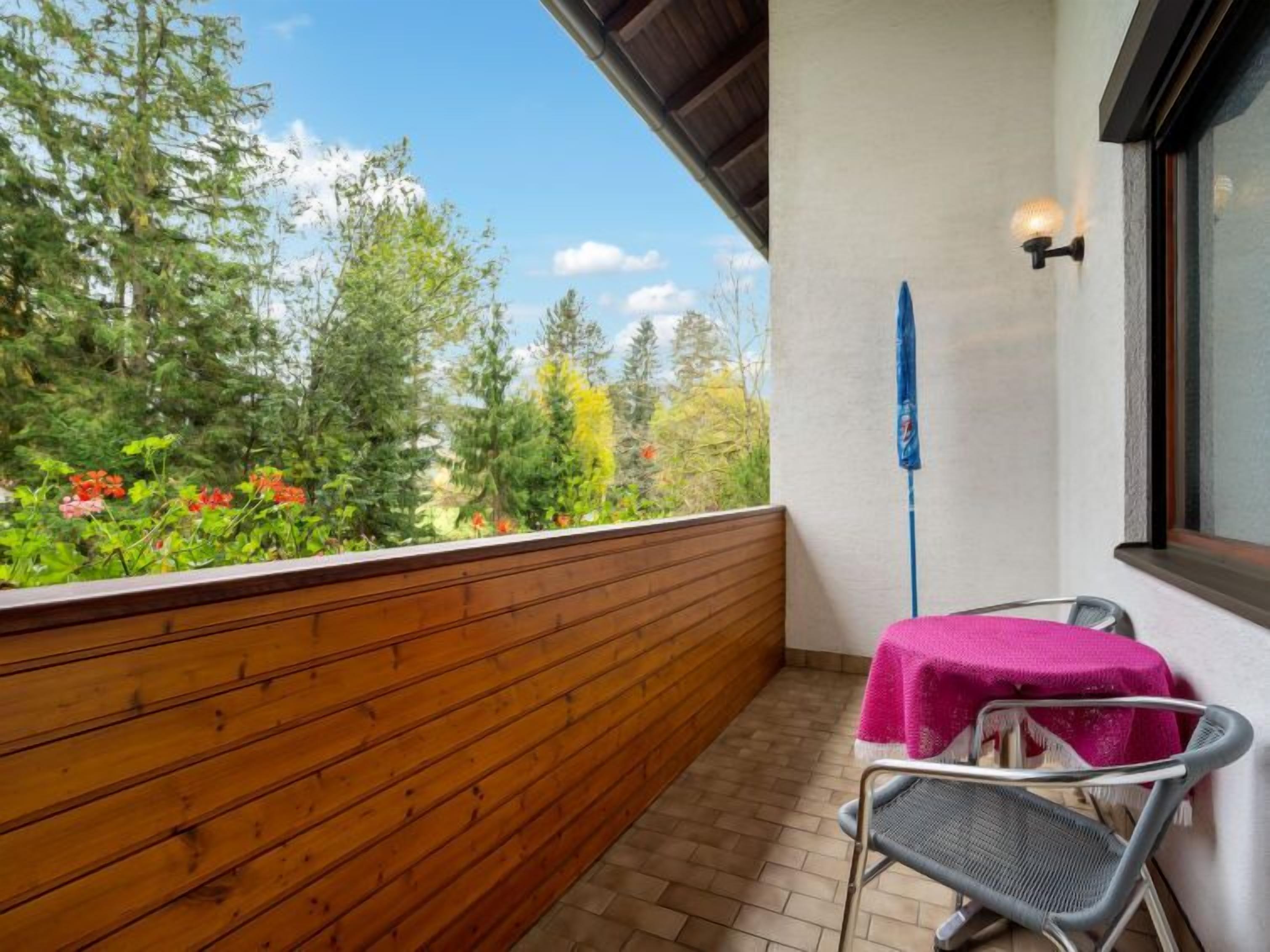 A balcony with wooden railings, a table with a pink tablecloth, and a chair.
