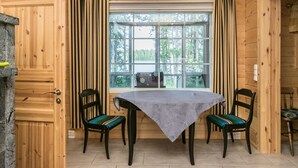 A wooden cabin interior with a dining table and chairs, a window with curtains, and a stone fireplace. - Villa eerola by Interhome (Juva)