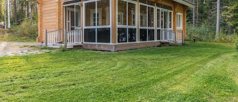 A wooden cabin with a large porch and a grassy yard.