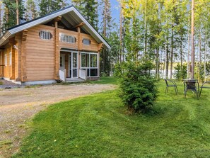 A wooden cabin with a porch and a small bush in the yard.