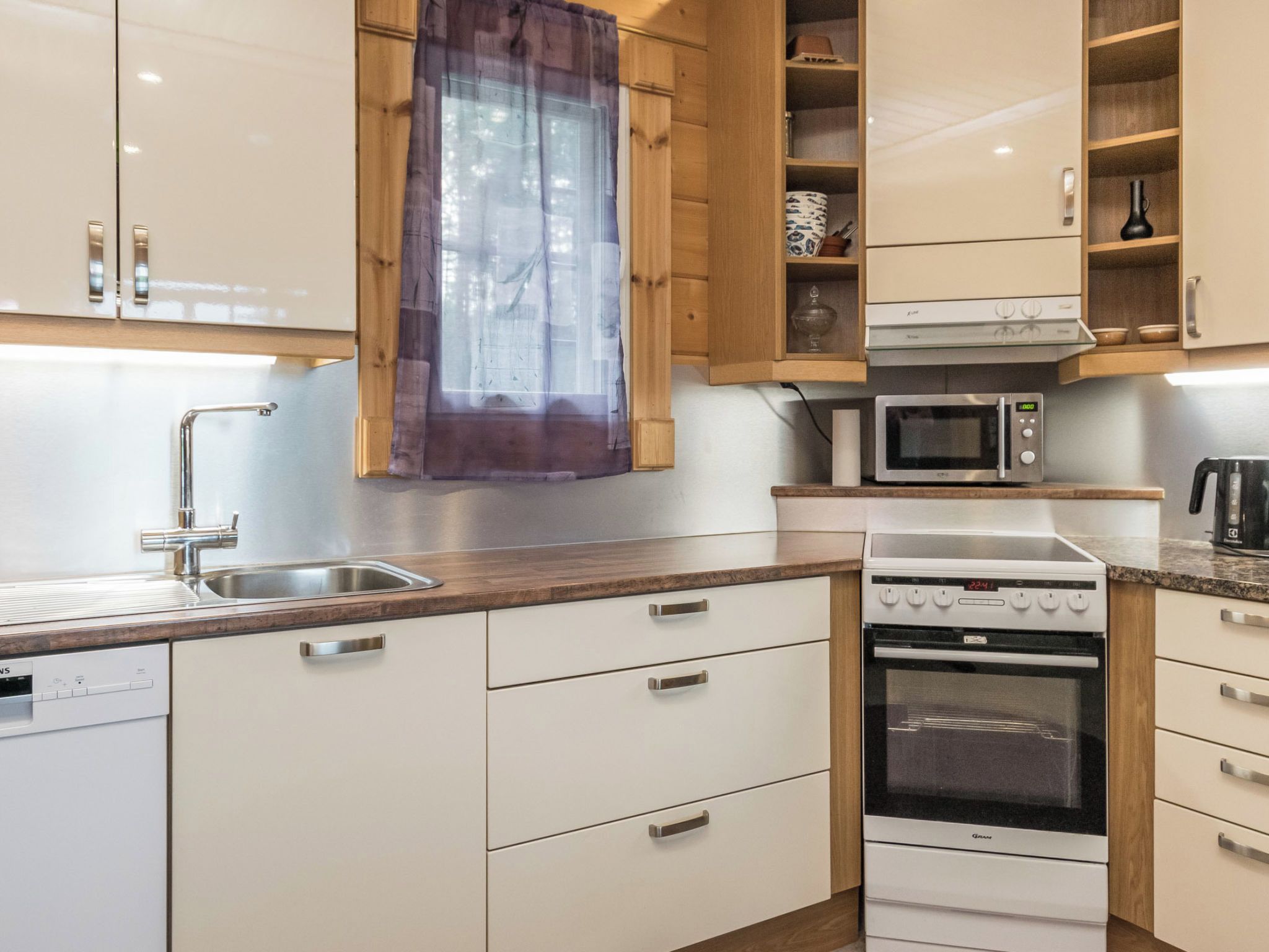 Une cuisine avec des meubles blancs, un évier en acier inoxydable, un four à micro-ondes et une cuisinière.