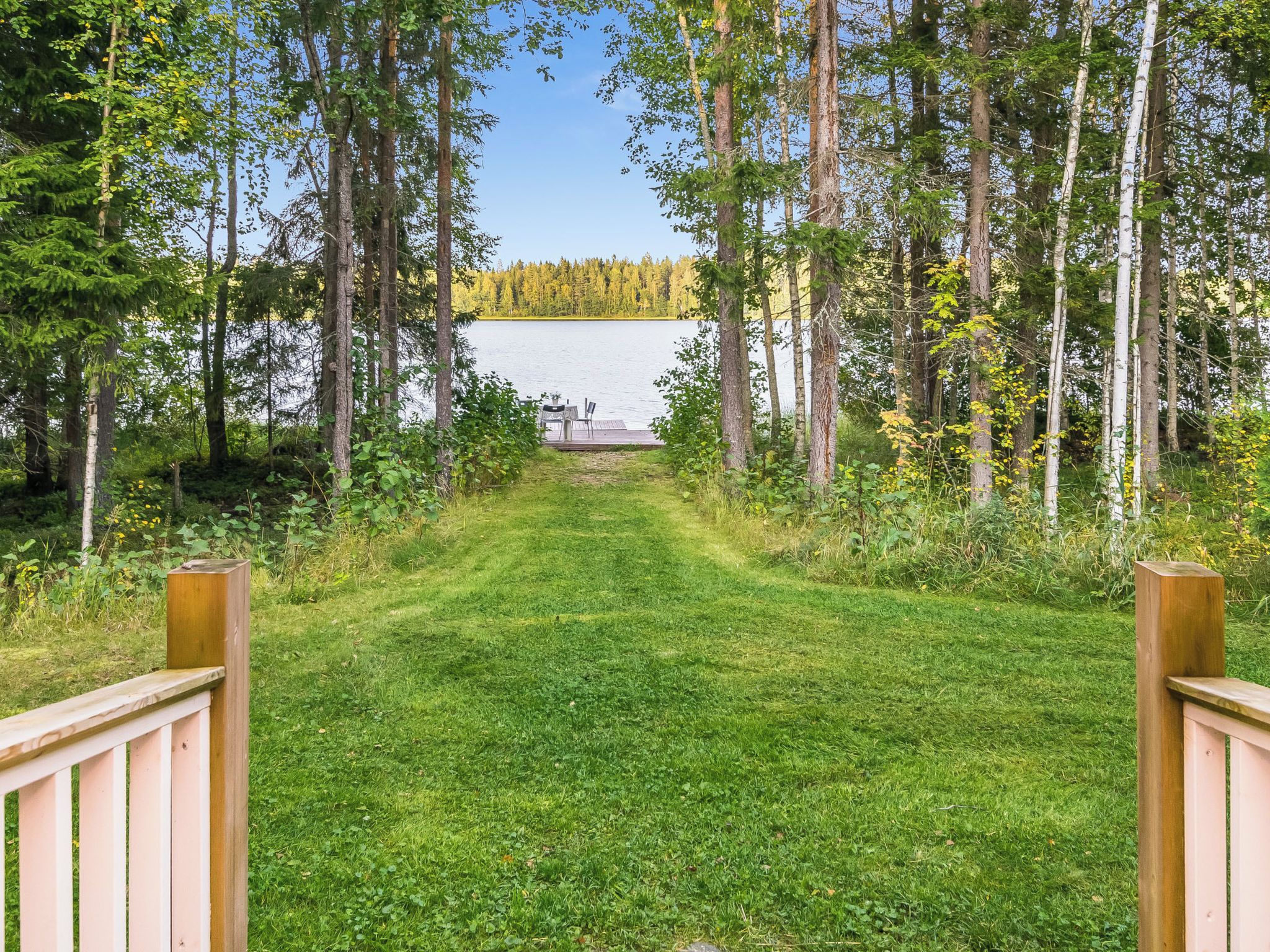 Un sentier qui mène à une zone au bord du lac, avec une terrasse en bois et des chaises.