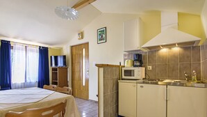A compact kitchen with a microwave, stove, and sink. There is a dining table with chairs and a television in the adjacent room.