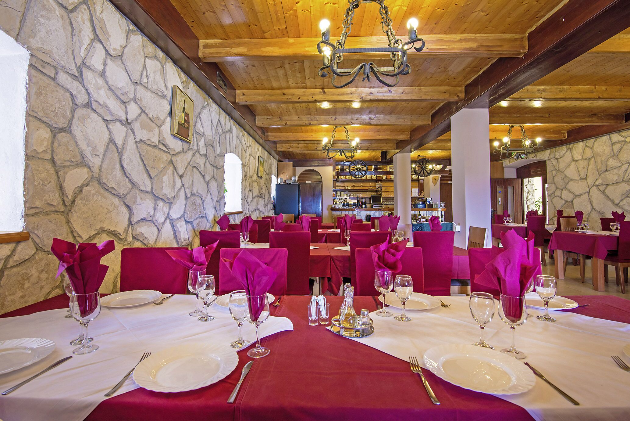 A restaurant with stone walls, wooden ceiling beams, and tables set with white tablecloths and red napkins.