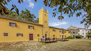 A courtyard with a yellow building, a clock tower, and a stone-paved area.