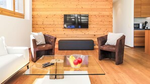 Una sala de estar moderna con una mesa de centro de vidrio, sillones de cuero y un televisor de pantalla plana montado en una pared de madera.