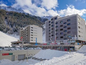 A modern hotel with multiple floors, a parking area, and a view of snow-covered mountains. - Rosablanche D 204 A by Interhome (Siviez-Nendaz)
