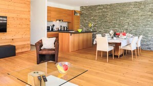 Una sala de estar moderna con una mesa de centro de vidrio, un sofá de cuero marrón y un comedor con una mesa y sillas blancas.