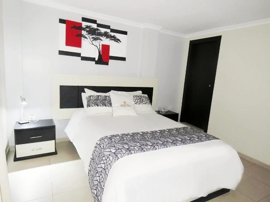 Un dormitorio ordenado con una cama, mesitas de noche y una obra de arte en la pared.