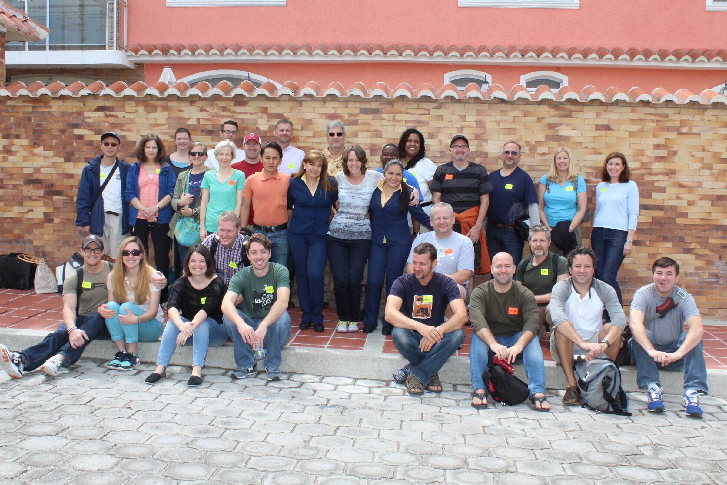 Un grupo de personas posando frente a un edificio con fachada de baldosas y pared de ladrillo.