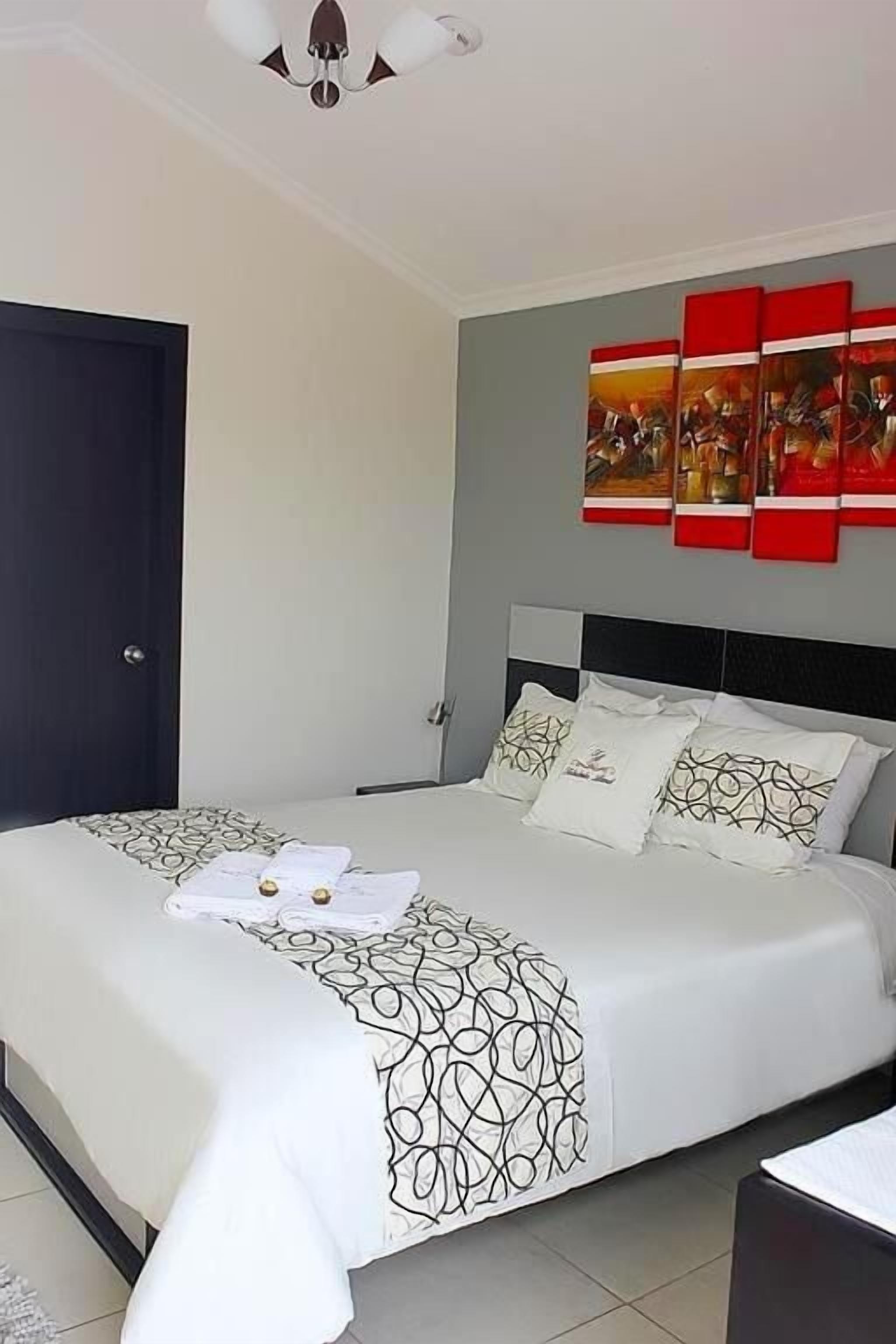 Una cama bien hecha con un edredón estampado, cabecera y un cuadro colgado en la pared.