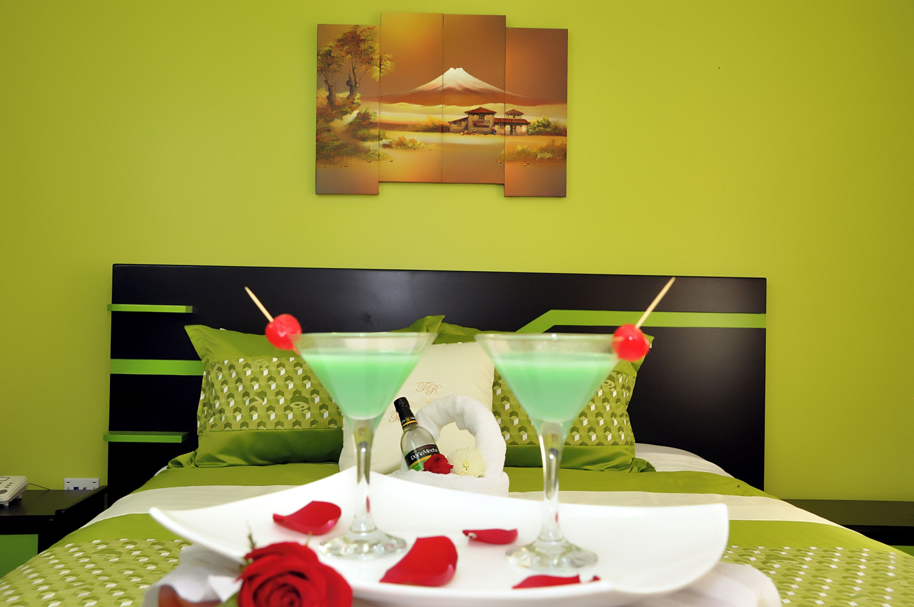 A bed with green bedding, a green wall, and a painting of a mountain.