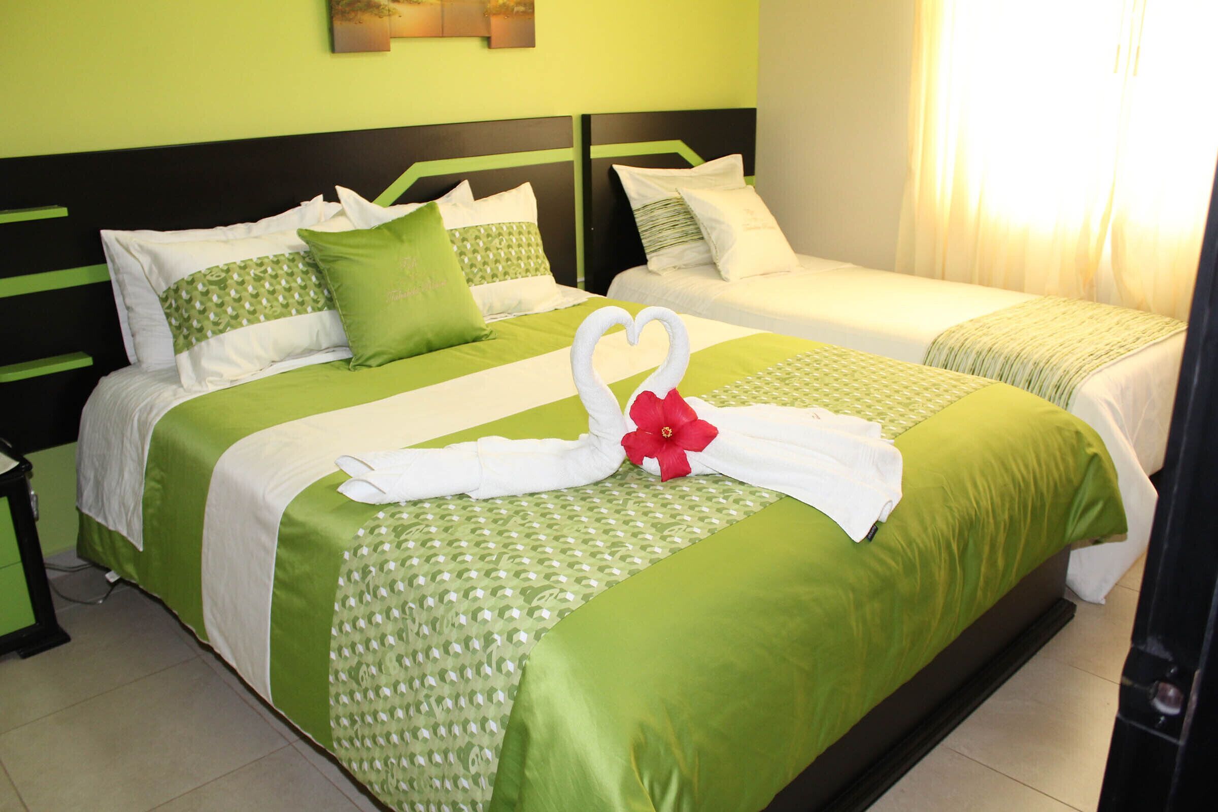 A hotel room with two beds, green bedding, white pillows, and a decorative swan made of towels.