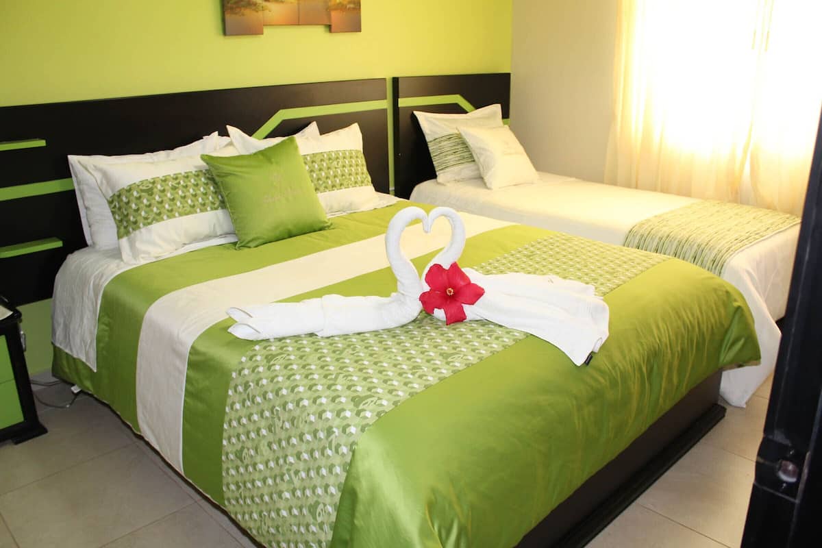 A hotel room with two beds, green bedding, white pillows, and a decorative swan made of towels.
