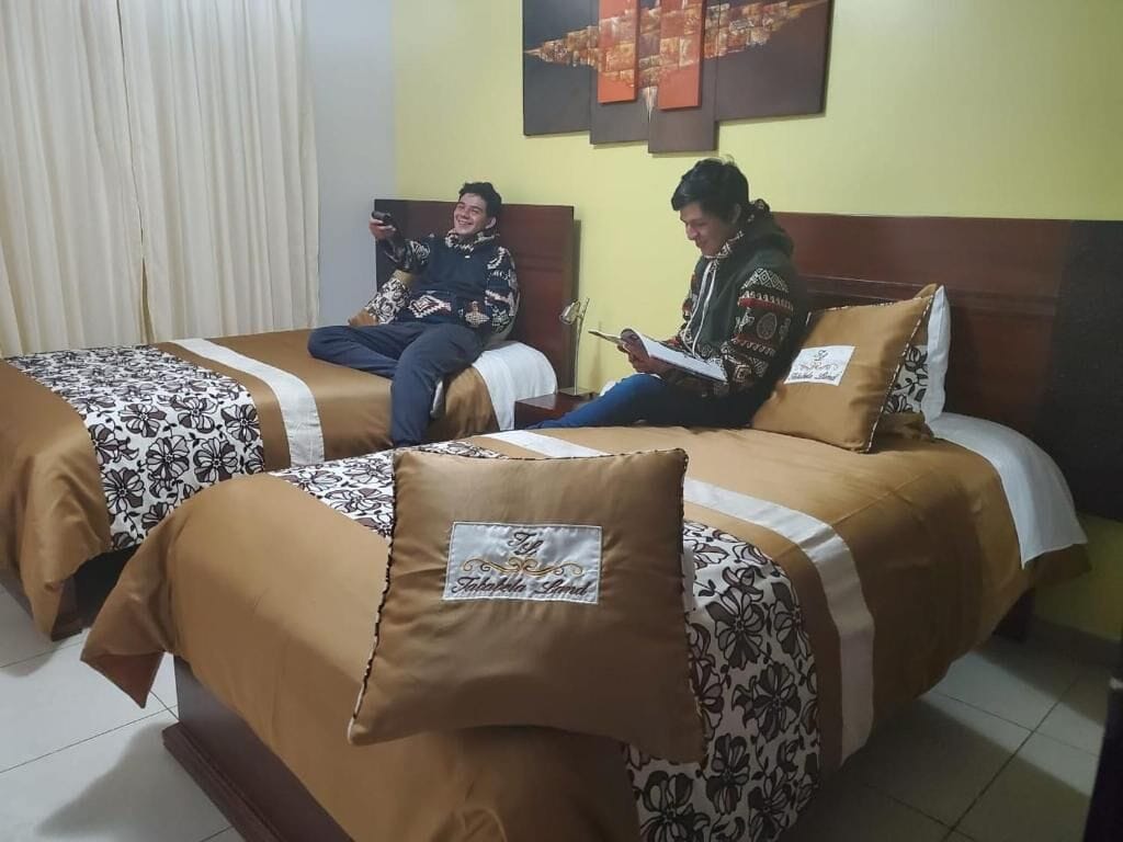Dos llits amb roba de llit estampada, un capçal de fusta i una paret amb un quadre de paisatge urbà.