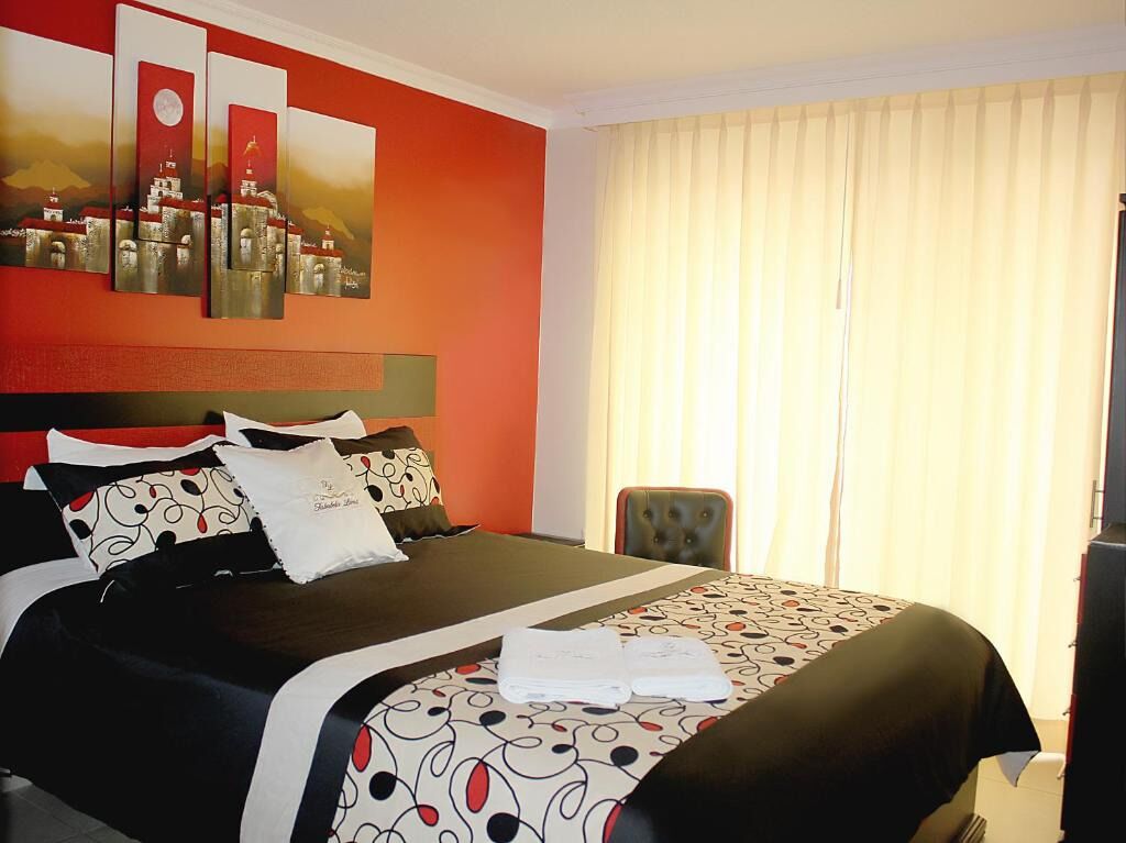 A hotel room with a bed, a headboard, a window with curtains, and a painting on the wall.