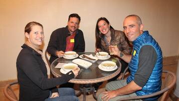 Un grupo de personas sentadas alrededor de una mesa redonda con cuencos de sopa, evocando un ambiente de comedor compartido.