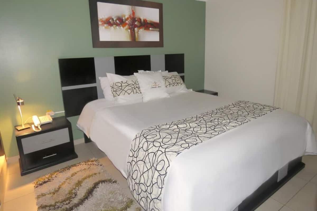 A neatly made bed with a patterned bedspread, a bedside lamp, and a framed picture on the wall.