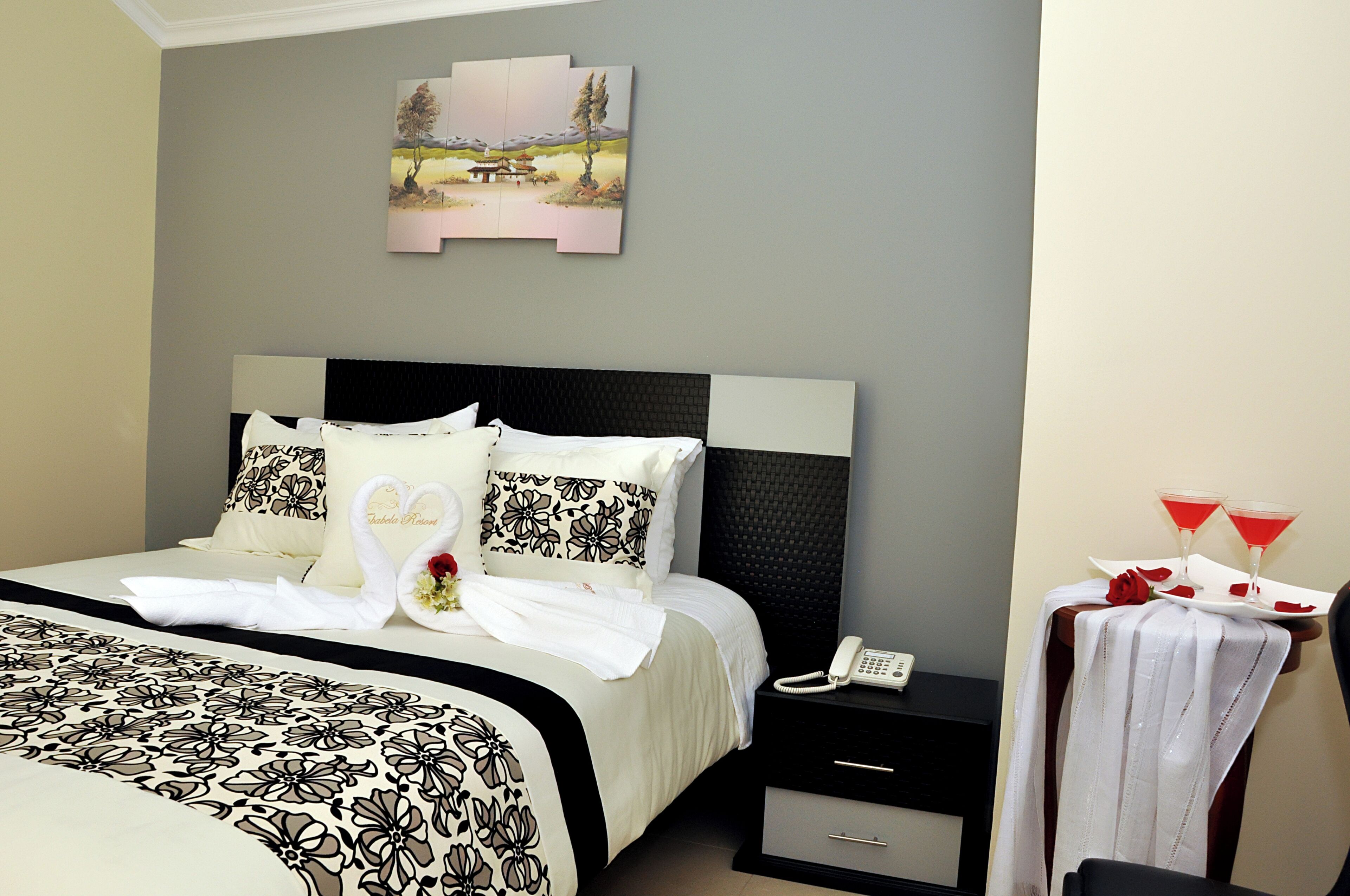 A neatly made bed with a floral bedspread, a nightstand with a phone, and a wall-mounted picture.