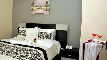 A neatly made bed with a floral bedspread, a nightstand with a phone, and a wall-mounted picture.