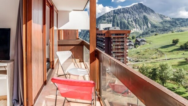 A balcony with a view of a mountain range, a TV, and two chairs. - Pegase Phenix by Interhome (Le Corbier)