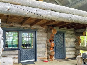A log cabin with a wooden porch, a large window, and a door with a decorative pattern.