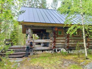 A log cabin with a metal roof, wooden porch, and a stone fireplace.