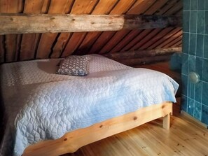 A wooden bed with a quilted mattress, a pillow, and a wooden headboard in a room with wooden beams and a tiled wall.