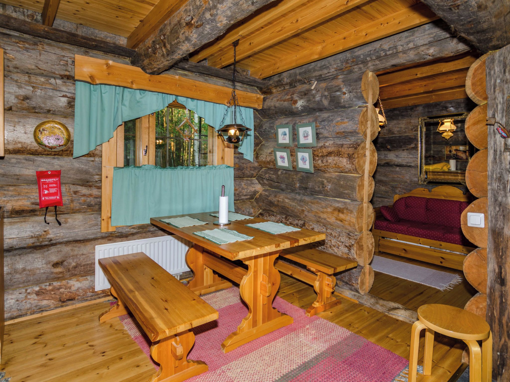 L’intérieur d’un chalet rustique en bois, avec une table à manger en bois, des bancs, un luminaire suspendu et un coin salon confortable.