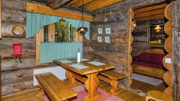 L’intérieur d’un chalet rustique en bois, avec une table à manger en bois, des bancs, un luminaire suspendu et un coin salon confortable.