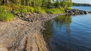 En klippefyldt kystlinje med klart vand, omgivet af tæt skov.
