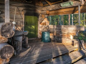 Une cabane rustique dotée d’une terrasse en bois, d’une porte verte et d’un mur en rondins.
