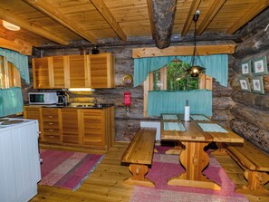 A rustic cabin interior with wooden walls, a kitchen area, a dining table with benches, and a window with curtains. - Köllölä 1 by Interhome (Nunnanlahti)