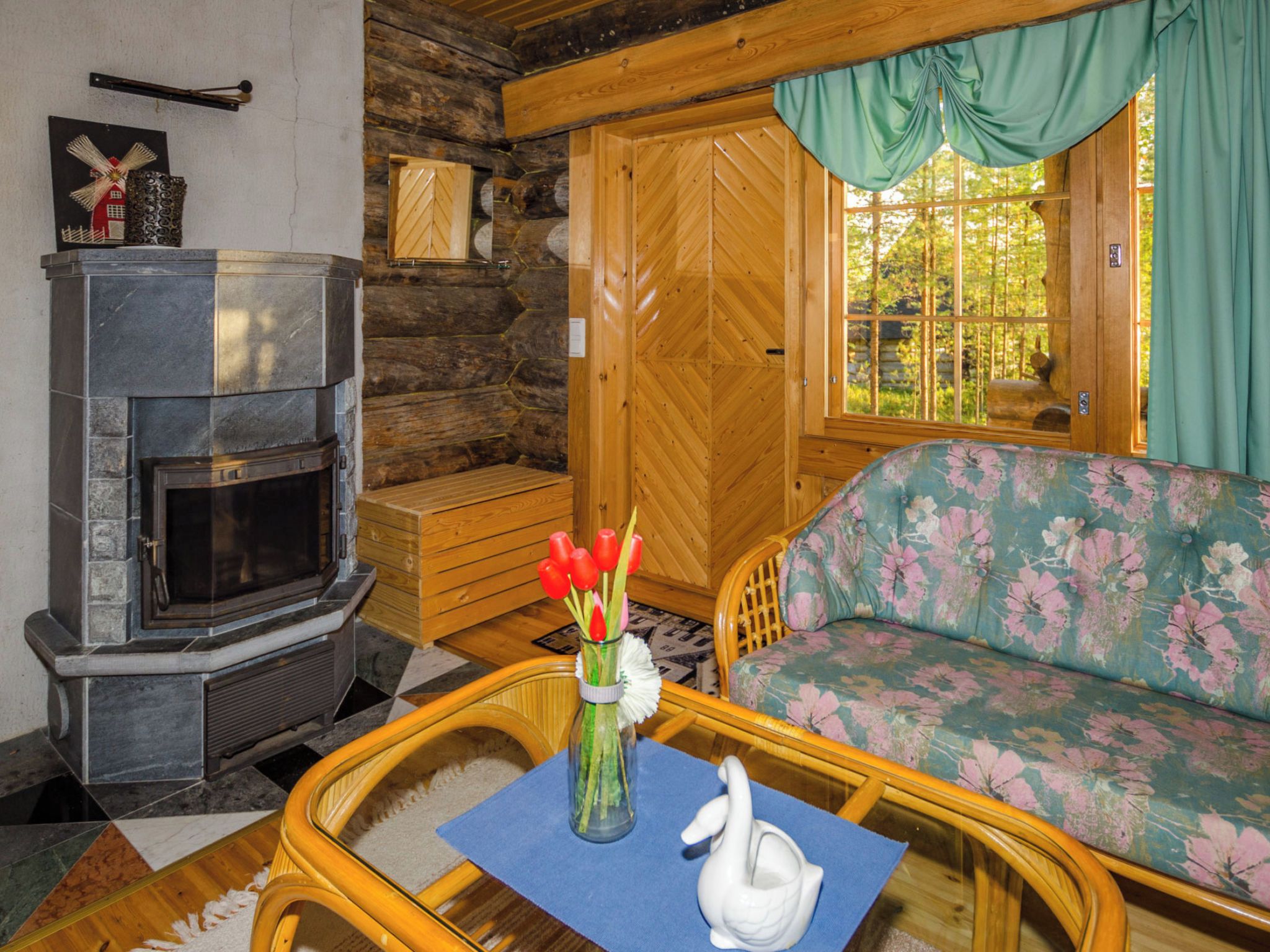 L’intérieur d’un chalet accueillant, avec une cheminée en pierre, des murs en bois, un canapé à motifs floraux et une table à manger en bois.