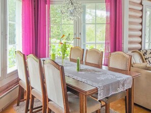 Un comedor con mesa de madera, sillas, mantel de encaje y una araña.