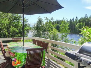 An outdoor deck with a table and chairs, a grill, and a view of a river and forest. - Käpälysmökki by Interhome (Nurmes)
