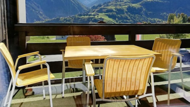 Een eetgedeelte met rieten stoelen en een tafel, met uitzicht op een bergachtig landschap.