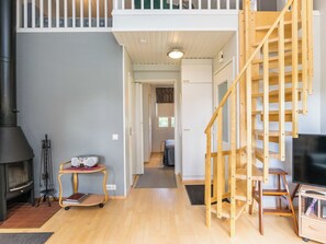 A spacious living area with a high ceiling, a fireplace, a wooden staircase, and a television. - Prokatti by Interhome (Sotkamo)