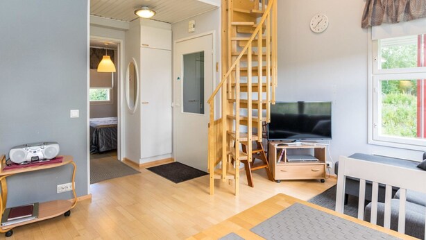 A spacious living area with a wooden staircase, a television, and a window with a view of greenery. - Prokatti by Interhome (Sotkamo)