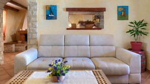 Un sofá color beige en una sala de estar con un arco de piedra, techo con vigas de madera y dos cuadros en la pared.