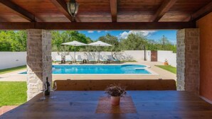 Un espacio al aire libre cubierto con piscina, sillones de descanso y sombrillas.
