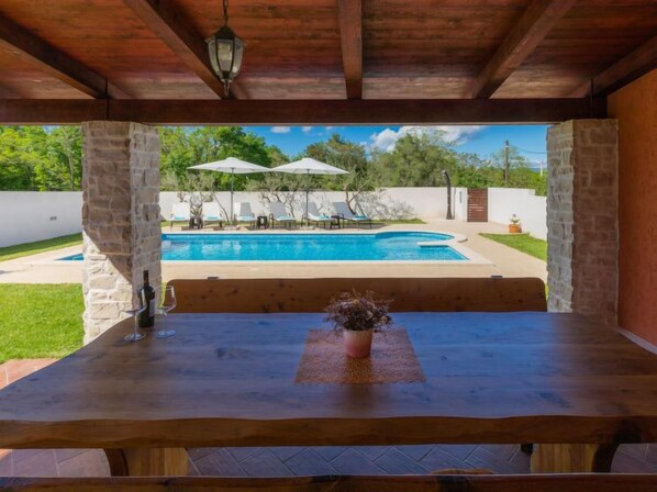 Un espace extérieur abrité comprenant une piscine, des chaises longues et des parasols.
