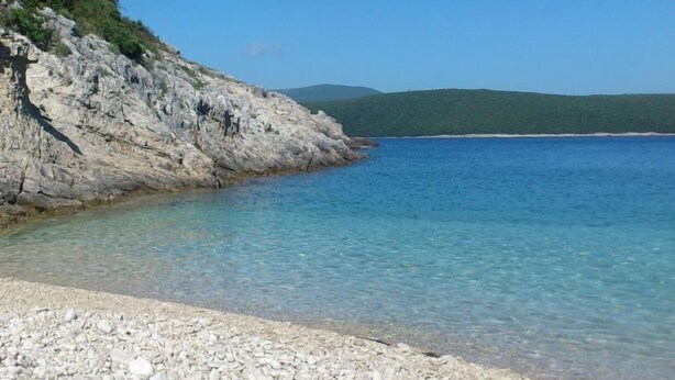 Costa rocosa con agua azul cristalina y una colina verde distante.