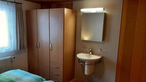 Quarto com cama, guarda-roupa, banheiro com pia e espelho, e janela com cortinas.