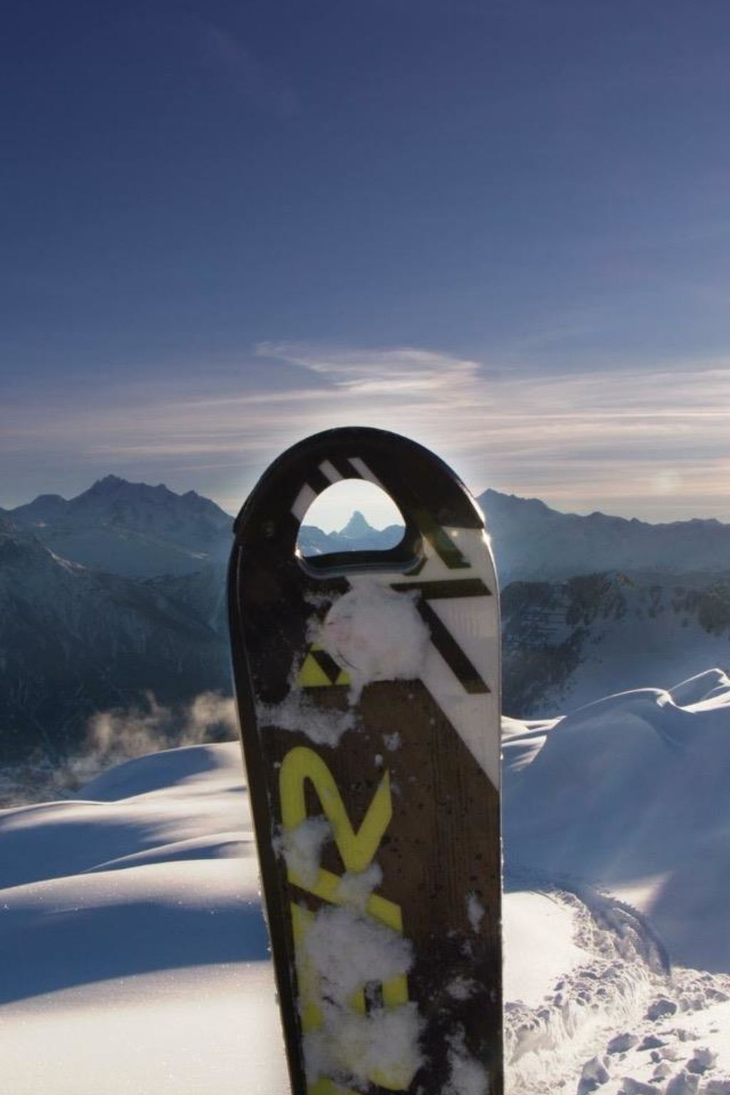 Ein Snowboard mit gelbem Logo vor verschneiter Bergkulisse.